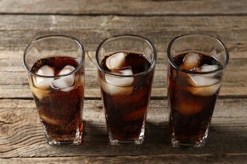 Refreshing cola with ice cubes in glasses on wooden table, closeup