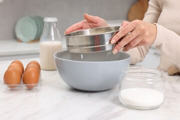 Making dough. Woman sifting flour into bowl at white table, closeup