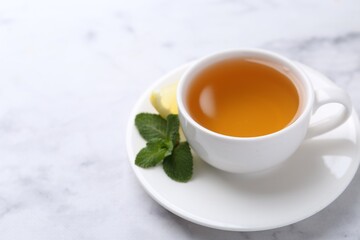 Aromatic mint tea in cup, fresh leaves and lemon on light table, closeup. Space for text