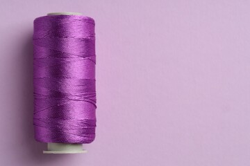 Spool of sewing thread on violet background, top view. Space for text