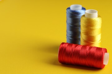 Different spools of sewing threads on yellow background, closeup. Space for text