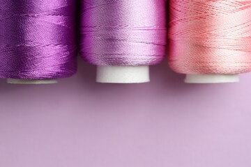 Different spools of sewing threads on violet background, flat lay. Space for text