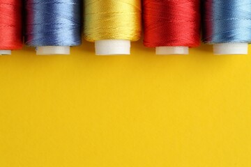 Different spools of sewing threads on yellow background, flat lay. Space for text
