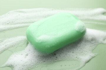 Soap bar with foam on green background, closeup