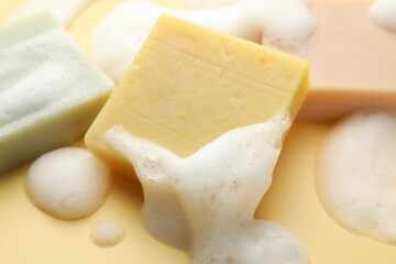 Soap bars with foam on yellow background, closeup