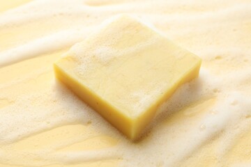 Soap bar with foam on yellow background, closeup
