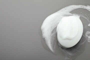 Soap bar with foam on grey background, top view. Space for text