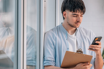 Fototapeta premium young man with mobile phone and documents next to the window