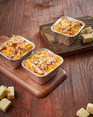 Three trays of baked casseroles are arranged on wooden boards with fresh cheese cubes scattered around them