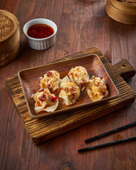Dumplings are arranged on a wooden platter alongside a small bowl of dipping sauce, exuding an...