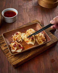 Freshly made dim sum arranged on a wooden platter with a side of dipping sauce, enjoyed with chopsticks in a warm restaurant ambiance