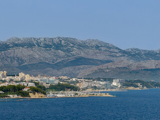 Obraz premium Split, Croatia - July 1, 2024: Zenta Marina yacht harbor in center of large landscape showing tall mountain range on horizon and an urban jungle around it. Tall apartment buildings and tourism-related