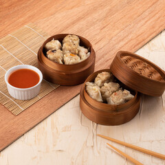 Steamed dumplings are presented in bamboo steamers alongside a small dish of spicy sauce, placed on a wooden surface