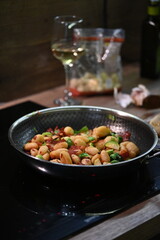 Gnocchi with vegetables sizzling in a black frying pan, set against a vibrant, colorful food background