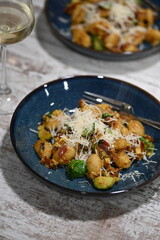 A close-up view of homemade gnocchi served on a blue plate, topped with freshly grated cheese