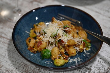 A close-up view of homemade gnocchi served on a blue plate, topped with freshly grated cheese