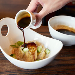Sauce is being poured over crispy snacks featuring cucumber pieces in a well-lit dining area with warm tones