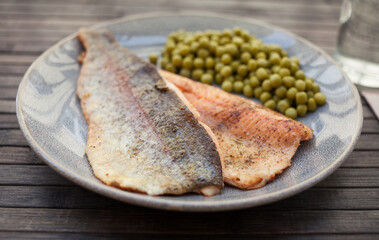 Top view of baked trout fillet served on plate with peas closeup