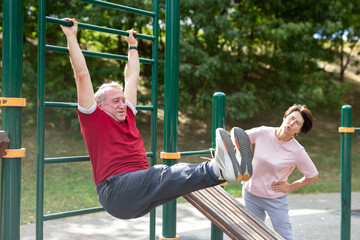 Elderly man and woman doing exercises on horizontal bars at outdoor sports ground