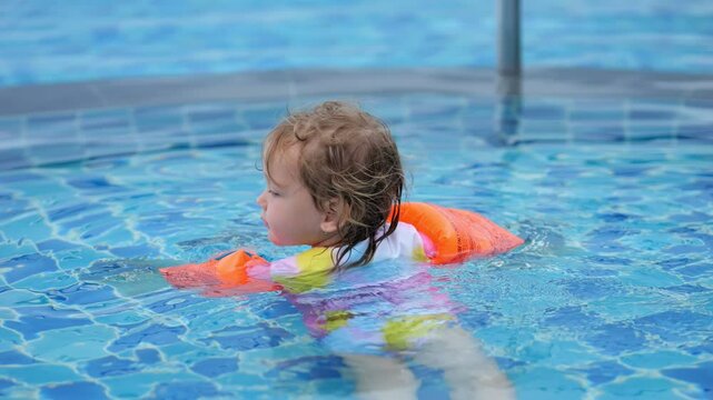 Young swimmer with floaties swims diligently making way through pool