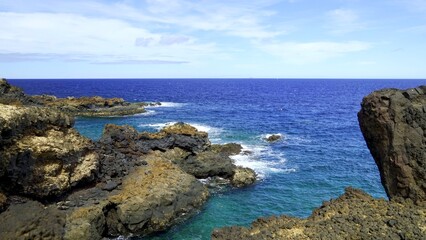 Turquoise waves crashing against the black volcanic rocks of the Charco del Palo coast in Lanzarote, Canary Islands, creating a dramatic contrast under a serene blue sky