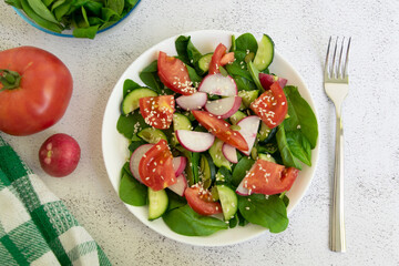 Raw fresh green healthy organic salad of spinach, cucumber, tomato and radish in white bowl on table top view on grey background.