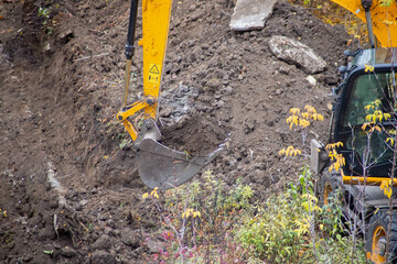 Close-up of an excavator bucket full of soil against the background of a dug trench during...
