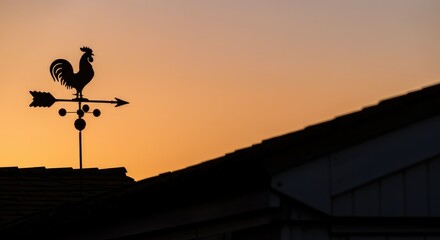 Naklejka premium Weathervane silhouette on roof at sunset, rooster-shaped