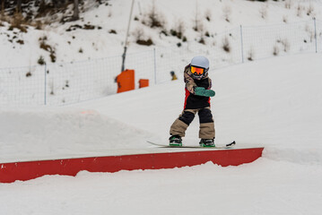 Children in snowpark in Dolomites Alps. Snow park box tricks. Snowboarder in park on a box. Winter jibbing in snwopark. Snowboard lessons on snowpark. Children learn to snowboard with an instructor.