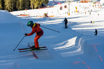 Children skiers in snowpark in Dolomites Alps. Snow park box tricks. Skiers in park on a box. Winter jibbing in snwopark. Ski lessons on snowpark. Children learn to ski with an instructor.