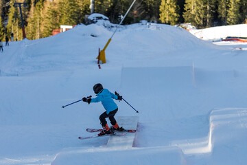 Children skiers in snowpark in Dolomites Alps. Snow park box tricks. Skiers in park on a box. Winter jibbing in snwopark. Ski lessons on snowpark. Children learn to ski with an instructor.