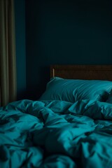 Cozy bedroom with rumpled teal bedding and soft pillows against a dark wall
