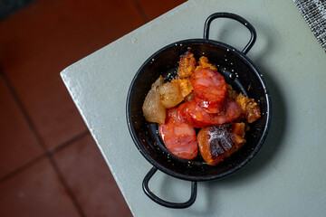 A small pot with traditional Alentejo sausages and fried pork lard, ready to be added to the classic tomato soup, showcasing authentic Portuguese cuisine.