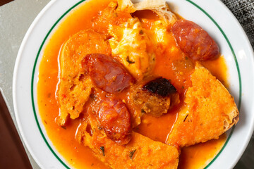 Traditional Portuguese tomato soup with fresh tomatoes, savory chorizo, poached egg, and slices of rustic bread, served in a cozy restaurant setting, embodying authentic local flavors.