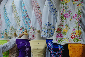 Various beautiful cotton clothes displayed at a fashion store. Colorful handmade embroidered fabrics with floral motifs and patterns. 