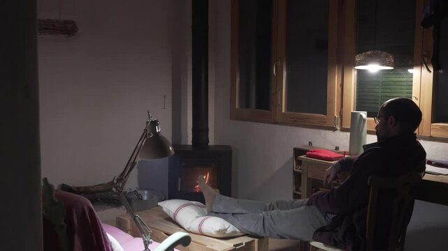 man in his forties sitting and relaxing in an idyllic rustic setting with wood-burning cooker at night