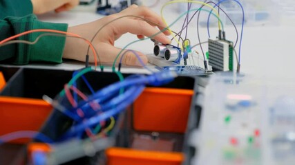 Close-up of a group of children assembling a robot from plastic parts programmed on a computer at a robotics school, the robot moves on a table. Creative kids working on the tech project at school. - Powered by Adobe