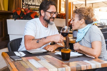 Two tourists enjoying a leisurely lunch at an outdoor restaurant, the man smiling as he offers a glass of red wine to the woman to smell its aroma, reflecting a moment of tasting and relaxation.