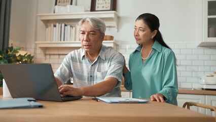 Obraz premium Grandmother comforting and supporting grandfather while looking at laptop show successful project and getting promotion. Happy senior businessman receive good news and talking to his wife. Myrmidon.