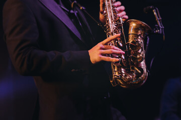 Obraz premium Concert view of saxophonist musician, saxophone sax player with vocalist and musical band during jazz orchestra show performing music on a stage in the scene lights, concert in a musical club hall
