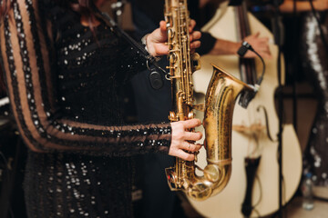 Fototapeta premium Concert view of female saxophonist musician, saxophone sax player woman with vocalist and musical band during jazz orchestra show, performing music on a scene in the stage lights in a musical club