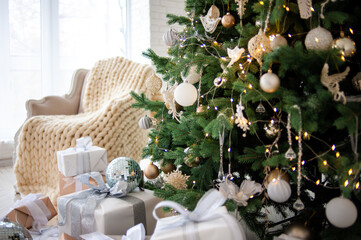 Elegant Christmas interior with a decorated tree in gold and white, wrapped gifts, a vintage beige sofa, and an armchair with a cozy knit blanket. Bright white walls create a festive, minimalism