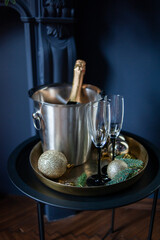 Stylish New Year celebration setup with a champagne bottle in a silver ice bucket, two elegant glasses, gold ornaments, and pine branches on a golden tray, set against a dark, luxurious background