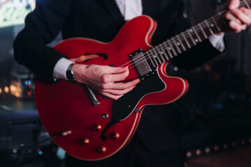 Obraz premium Concert view of an electric guitar player with vocalist and rock band performing in a club, male musician guitarist on stage with audience in a crowded concert club hall arena, hands on a guitar