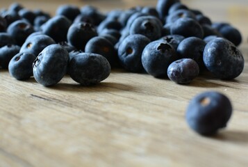 Fresh bilberries spread on wooden table side view. A lot of blue berries dropped on wooden table close up macro