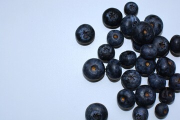 Fresh bilberries spread on white table close up top view macro. A lot of blue berries on white surface.