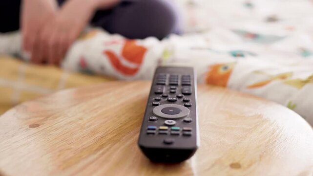 Tv remote closeup as child watches TV at home. Entertainment for children concept. School girl watches cartoons at home.