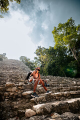 Turista joven latino, sentado con su cámara en las escaleras de una pirámide, admirando el paisaje de la selva y las ruinas que lo rodean, en Cobá, México