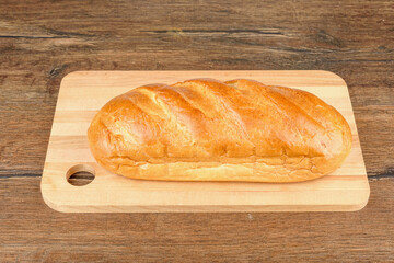 A whole loaf of white bread on a wooden cutting board.