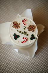 Delicate festive Christmas children's cake, decorated with gingerbread men and candy canes in a Christmas style of a beautiful beige color, prepared for a 7-month-old baby